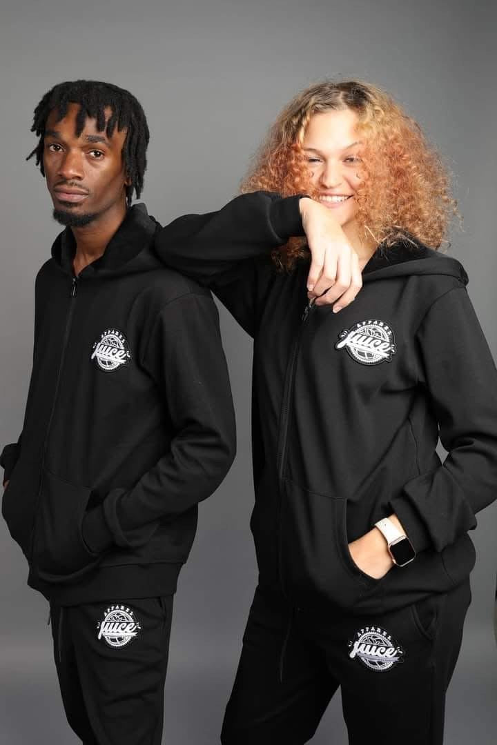 Two people wearing black hooded jackets with a juice logo on chest and upper leg of pant a gray background
